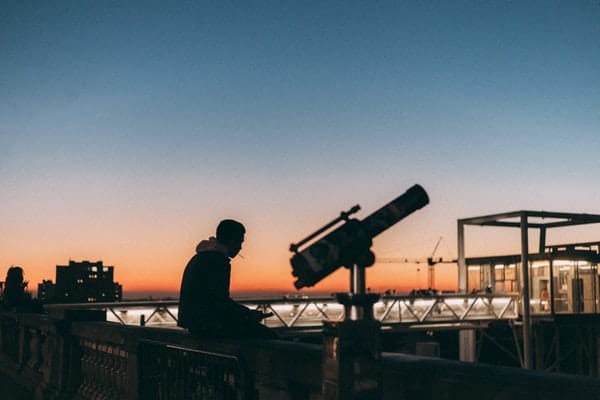 Man sitting on top of building near a telescope
